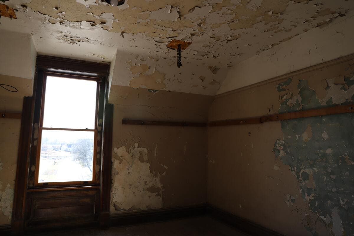 Une chambre avec des murs moisis et une fenêtre.