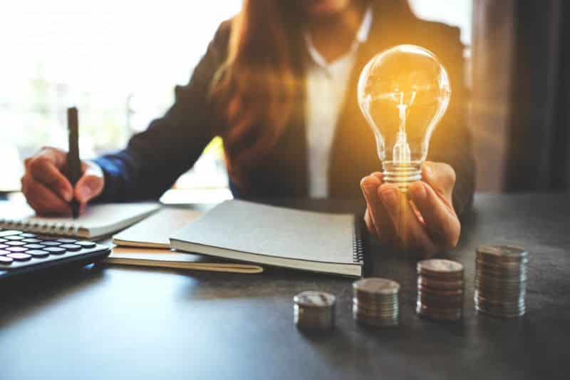 Une femme tenant une ampoule et des pièces de monnaie à un bureau.