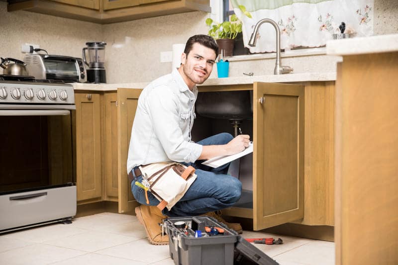 Un plombier travaillant sur un évier dans une cuisine.