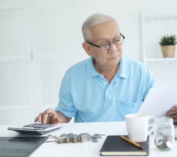 Serious man sitting at table near utility bill and calculating expenses