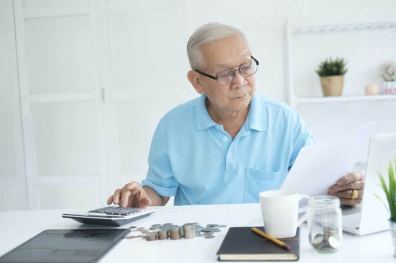 Serious man sitting at table near utility bill and calculating expenses