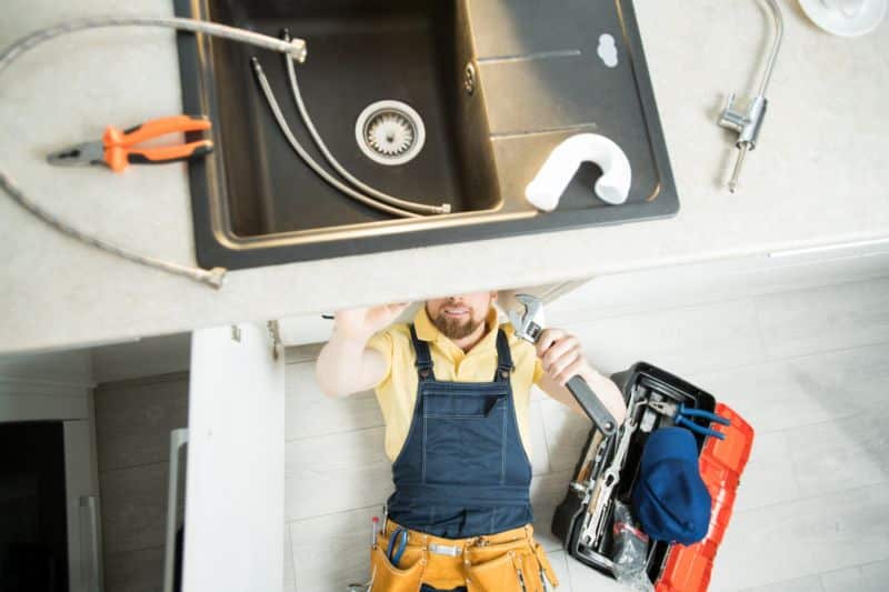 Plumber repairing pipe in kitchen