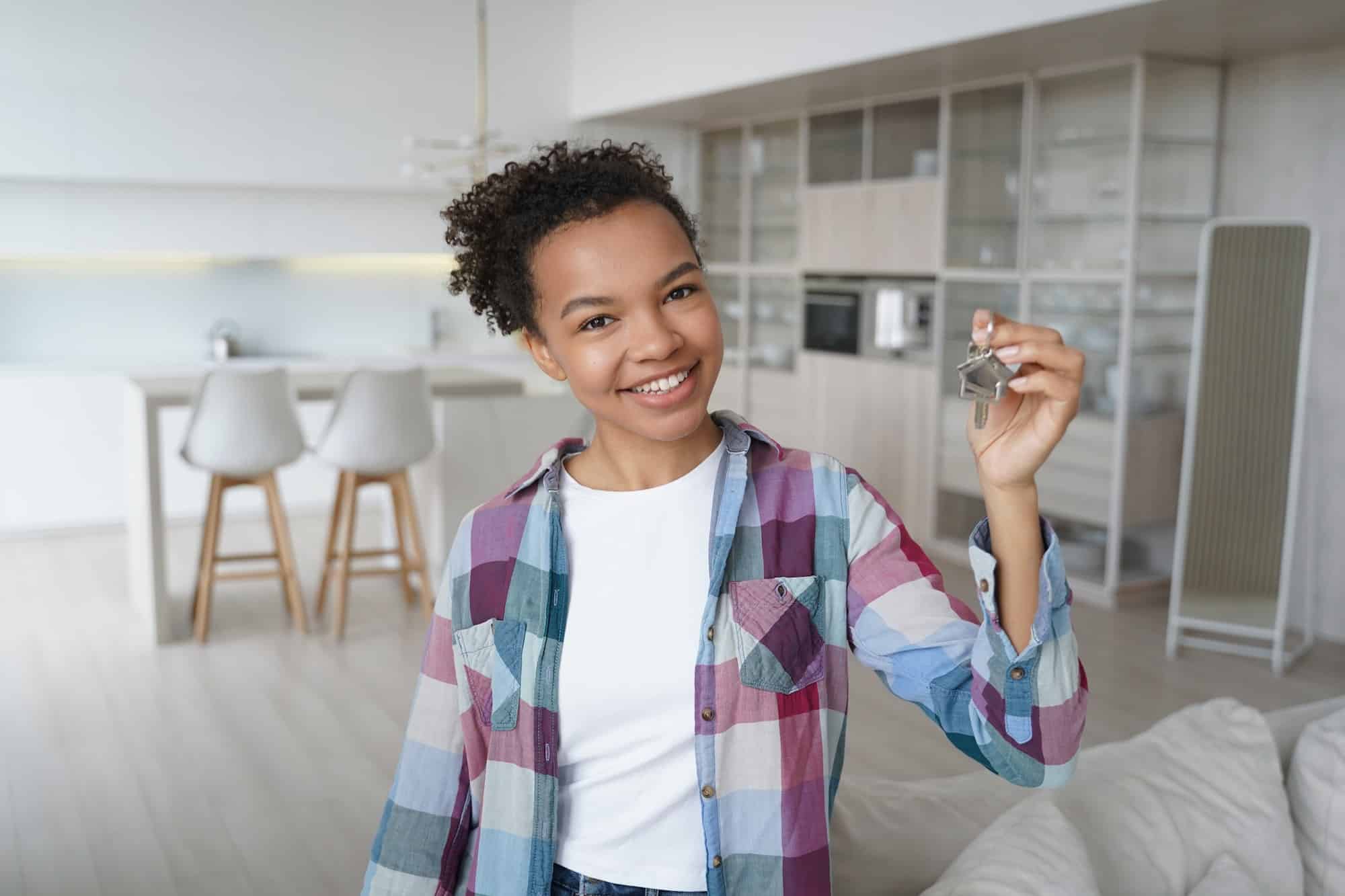 Happy young biracial girl homeowner tenant shows key to new house. Relocation, real estate rent