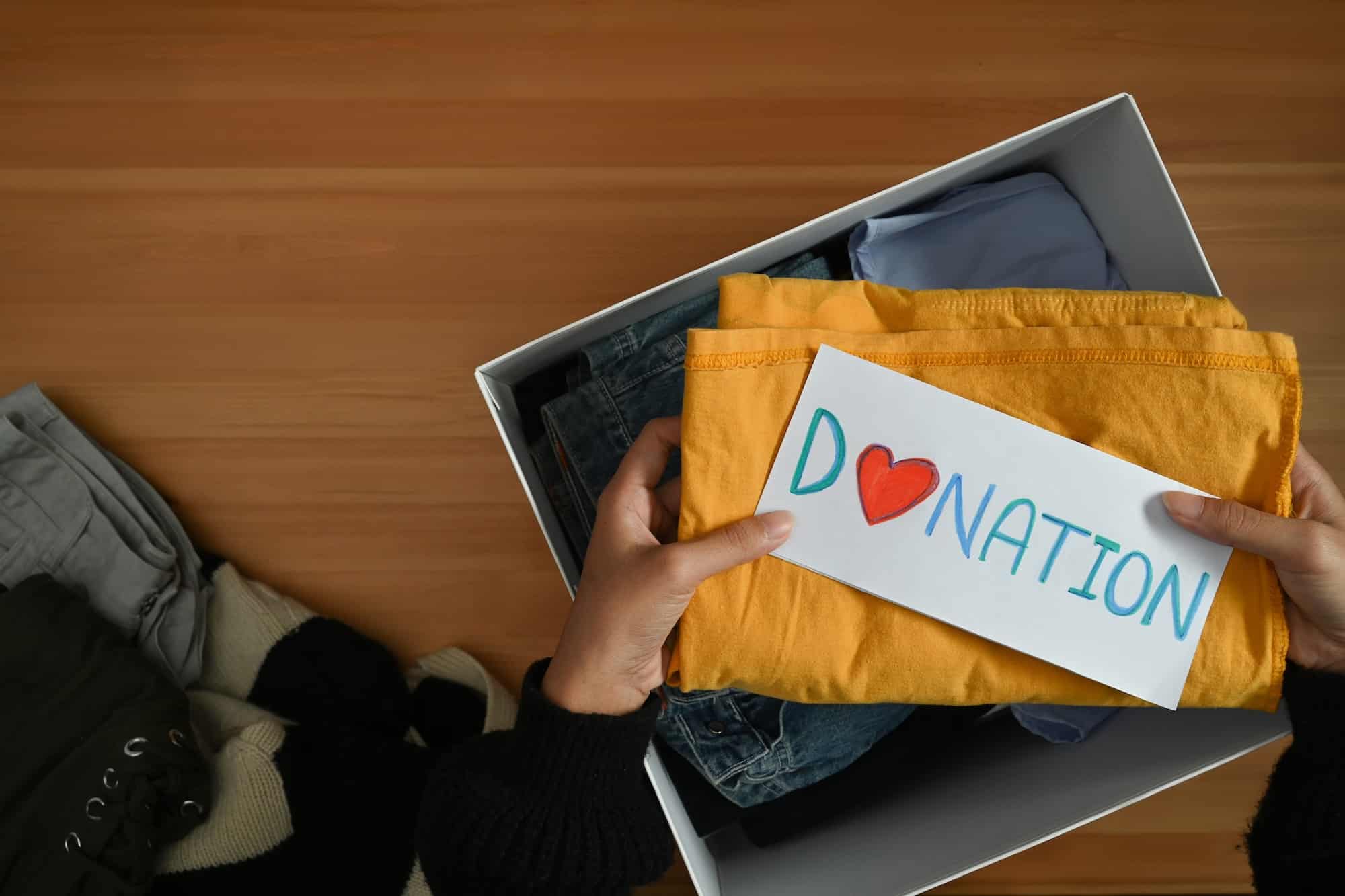 Top view of Donation box with clothes on wooden table. Charity, donation and reuse recycle concept.