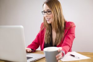 Une Femme à Lunettes Est Assise à Un Bureau Avec Un Ordinateur Portable Et Une Tasse De Café.