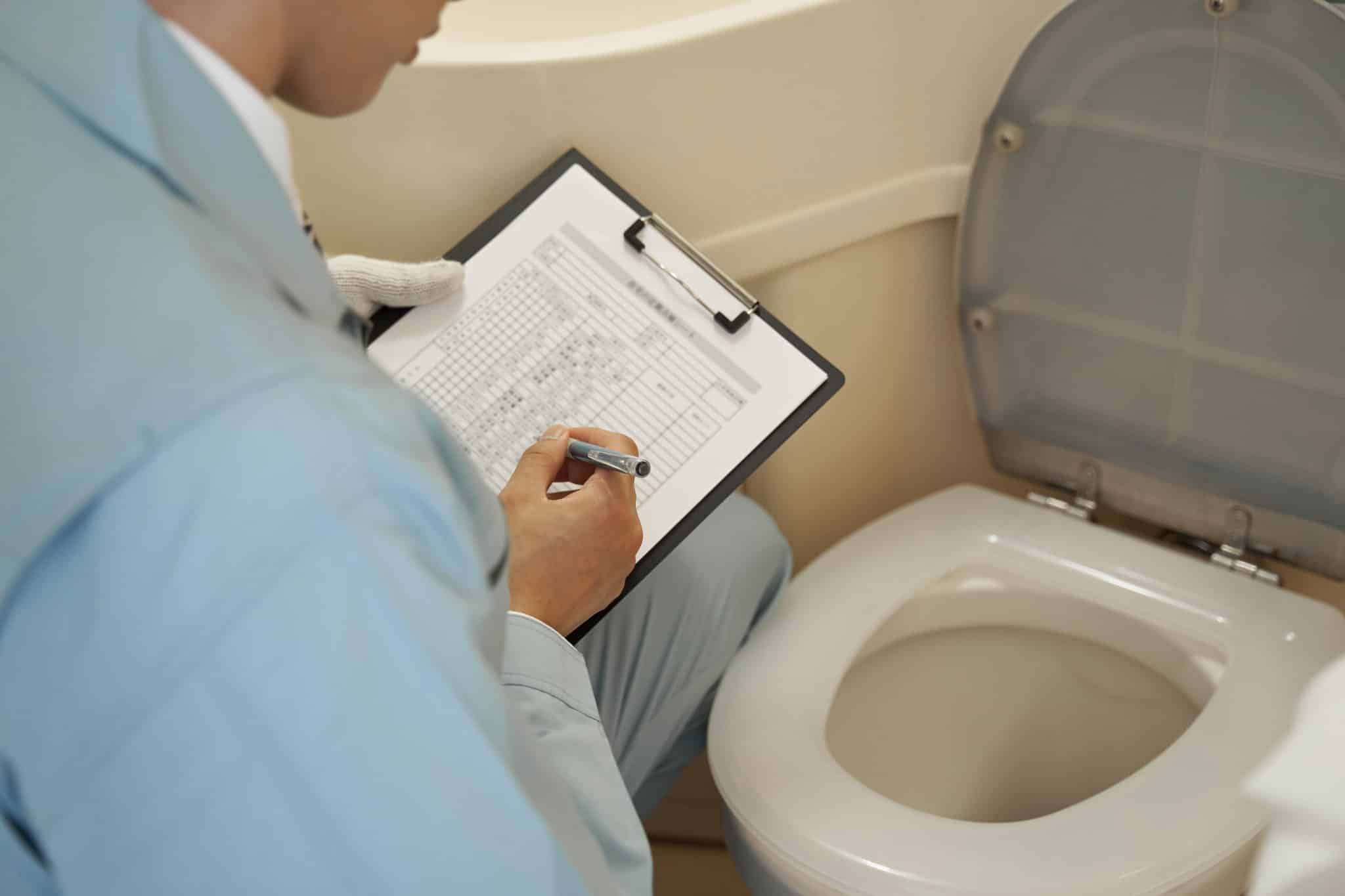 Un Homme Tenant Un Presse Papiers Devant Les Toilettes.