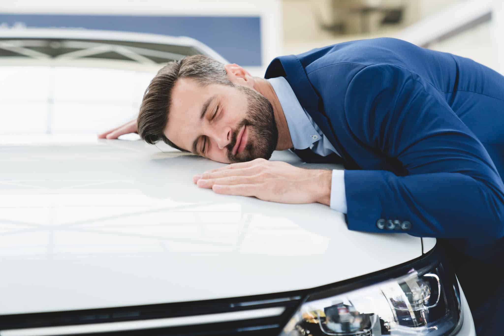 Un Homme En Costume Dort Sur Le Capot D’une Voiture.