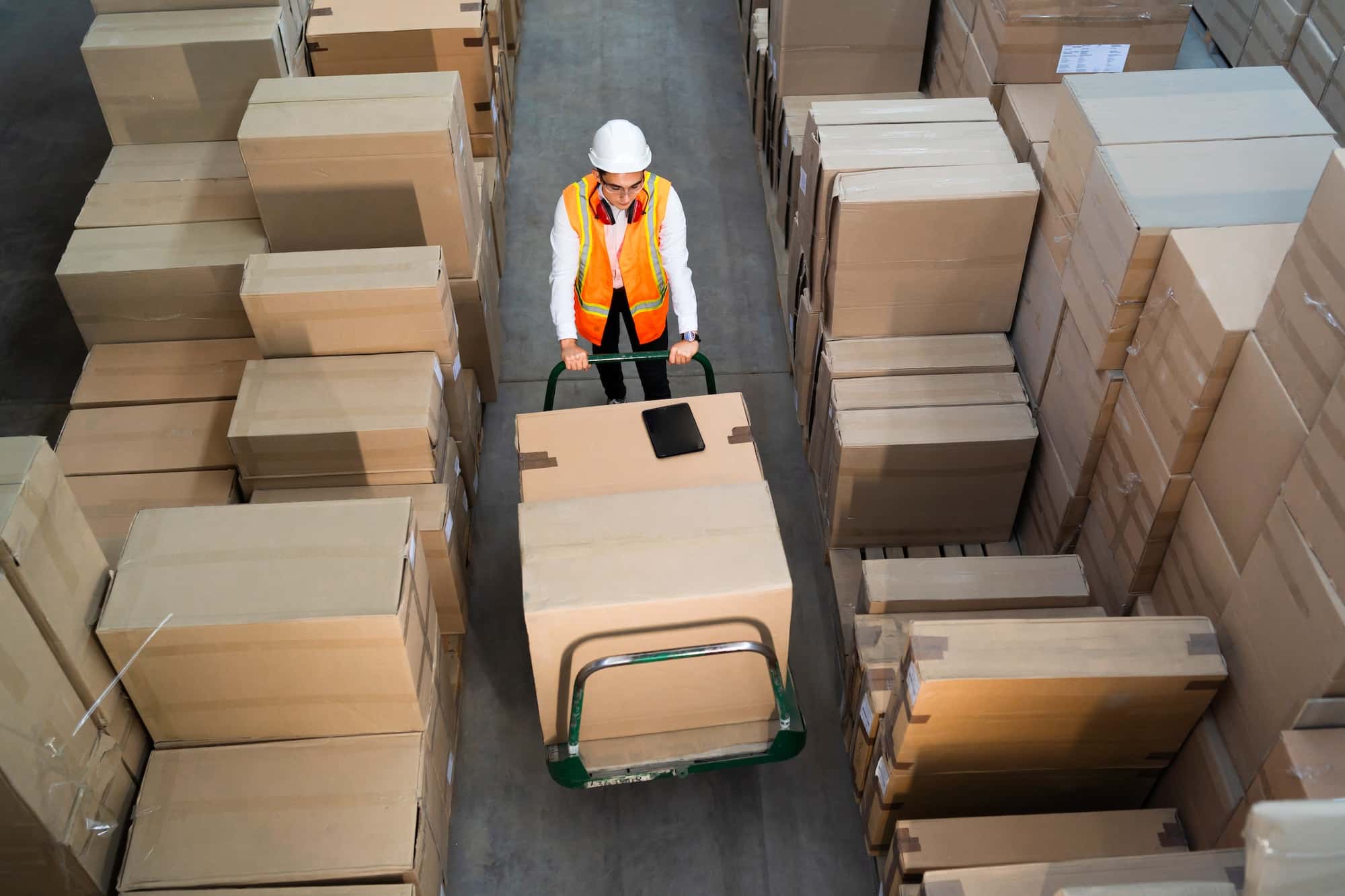Un ouvrier poussant un chariot rempli de cartons dans un entrepôt.