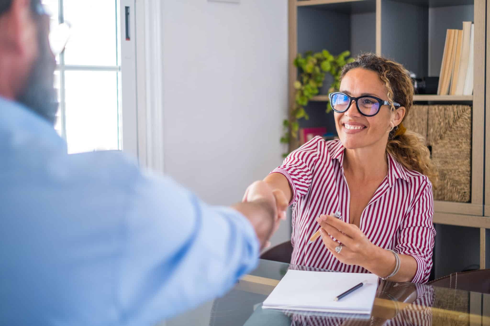 Une Femme Serre La Main D’un Homme Assis à Un Bureau.