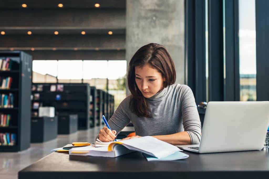 Une Femme Assise à Un Bureau Dans Une Bibliothèque Avec Un Ordinateur Portable.