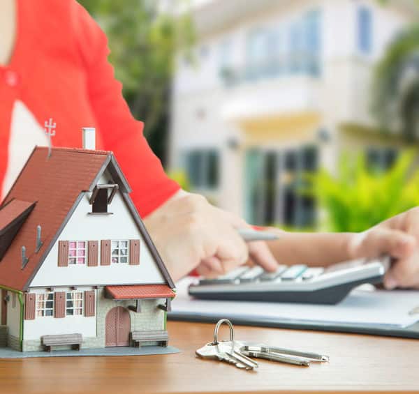 Une Femme Tient Une Calculatrice Et Un Modèle De Maison Sur Une Table.