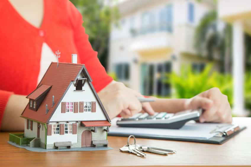 Une Femme Tient Une Calculatrice Et Un Modèle De Maison Sur Une Table.