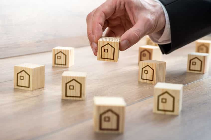 Un Homme En Costume Place Des Blocs De Maison En Bois Sur Une Table.