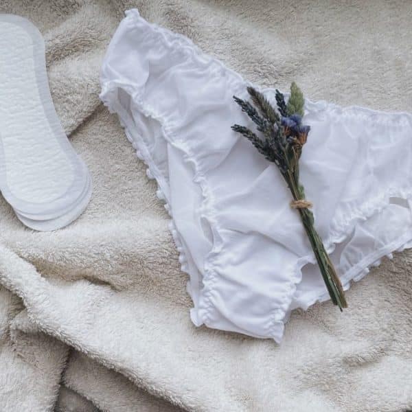 Une Paire De Culottes Blanches Et Une Fleur De Lavande Sur Une Couverture Blanche.