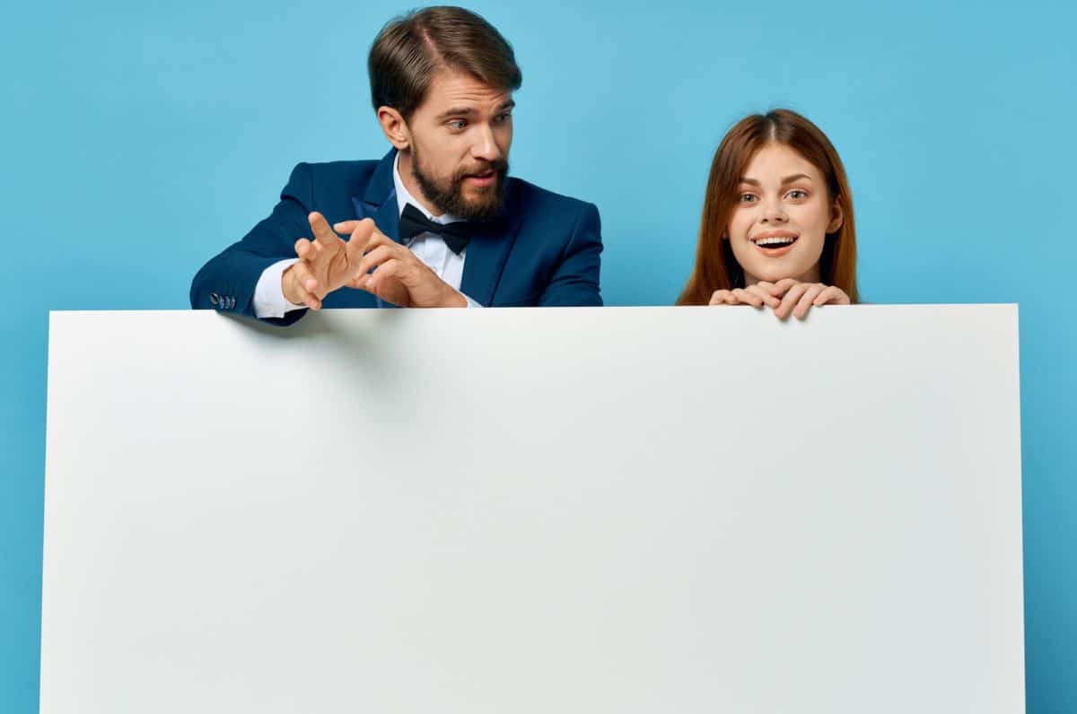 Un Homme Et Une Femme Tiennent Un Tableau Vierge Sur Un Fond Bleu.