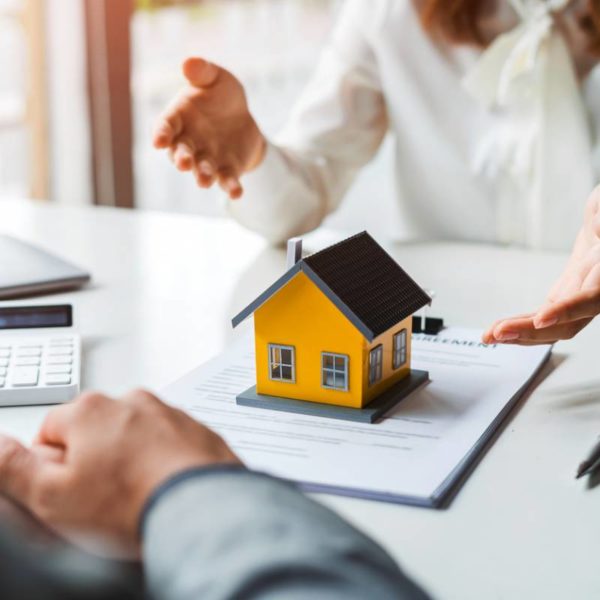 Deux Personnes Tenant Un Modèle De Maison Devant Une Calculatrice.