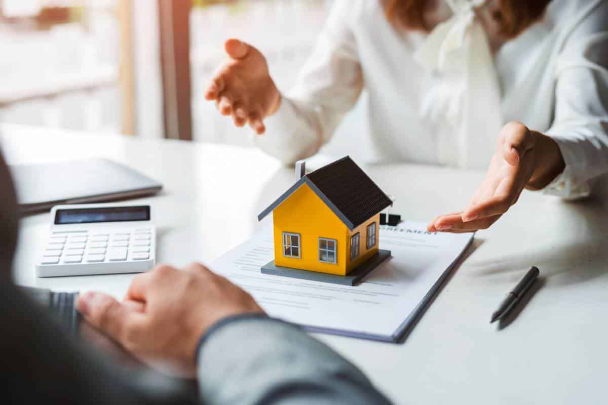 Deux Personnes Tenant Un Modèle De Maison Devant Une Calculatrice.