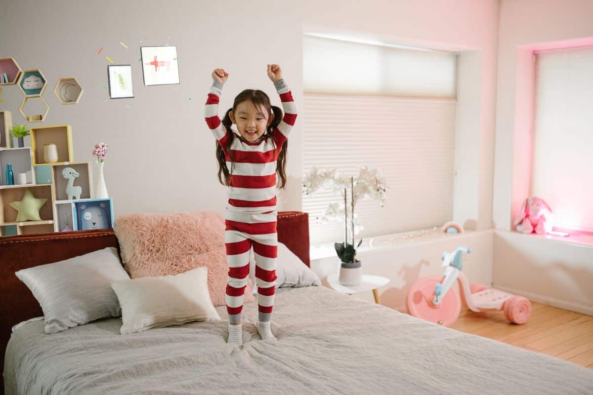 Une fille debout sur son lit dans une chambre d'enfant au style ludique.