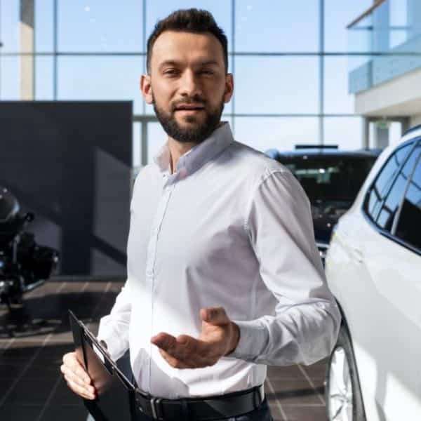 Un Homme Debout à Côté D’une Voiture Dans Une Salle D’exposition.
