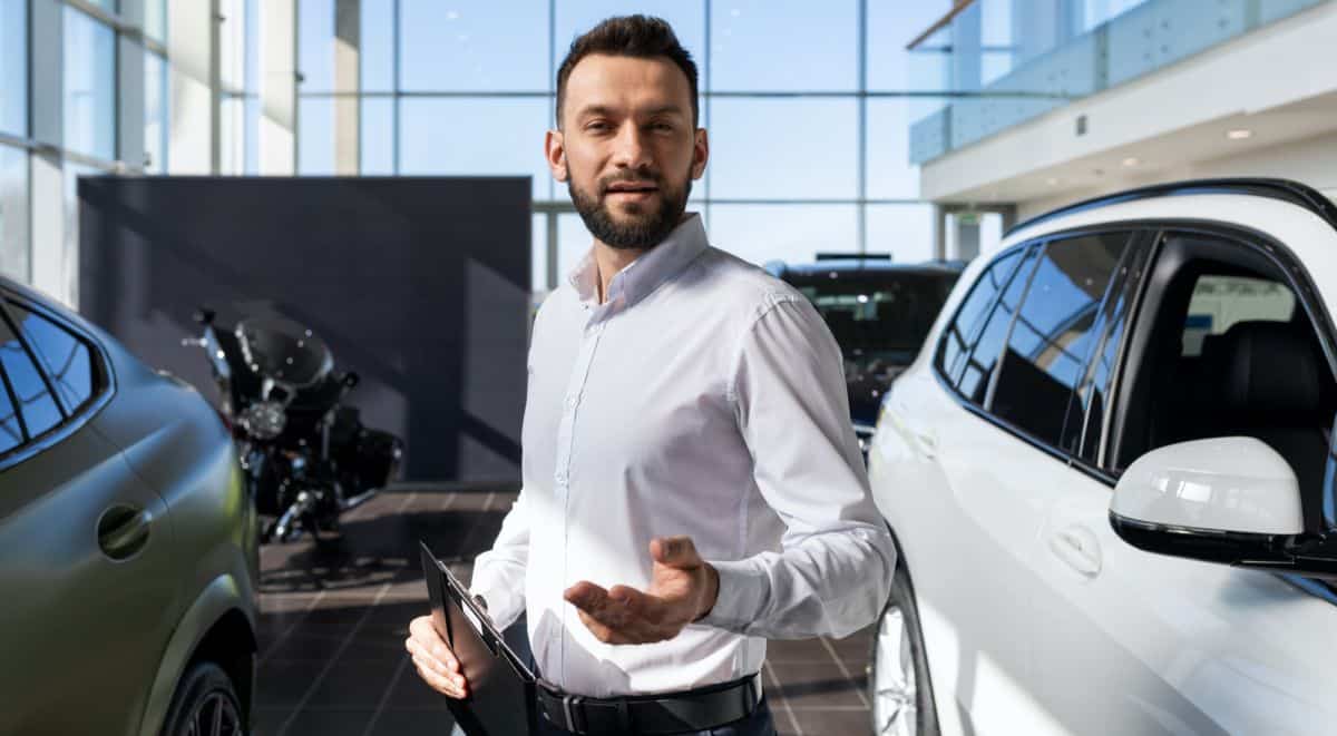 Un Homme Debout à Côté D’une Voiture Dans Une Salle D’exposition.