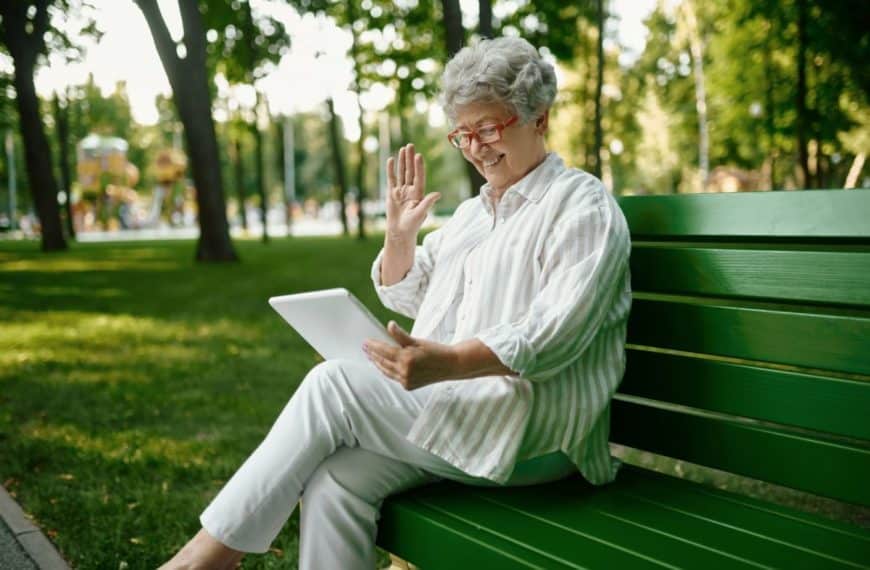 Une Femme âgée Est Assise Sur Un Banc De Parc Avec Une Tablette.