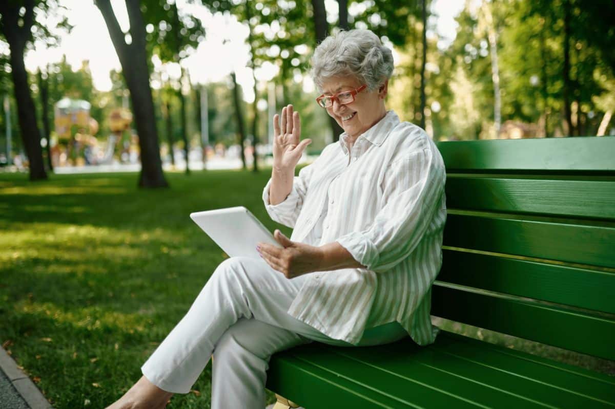 Une Femme âgée Est Assise Sur Un Banc De Parc Avec Une Tablette.