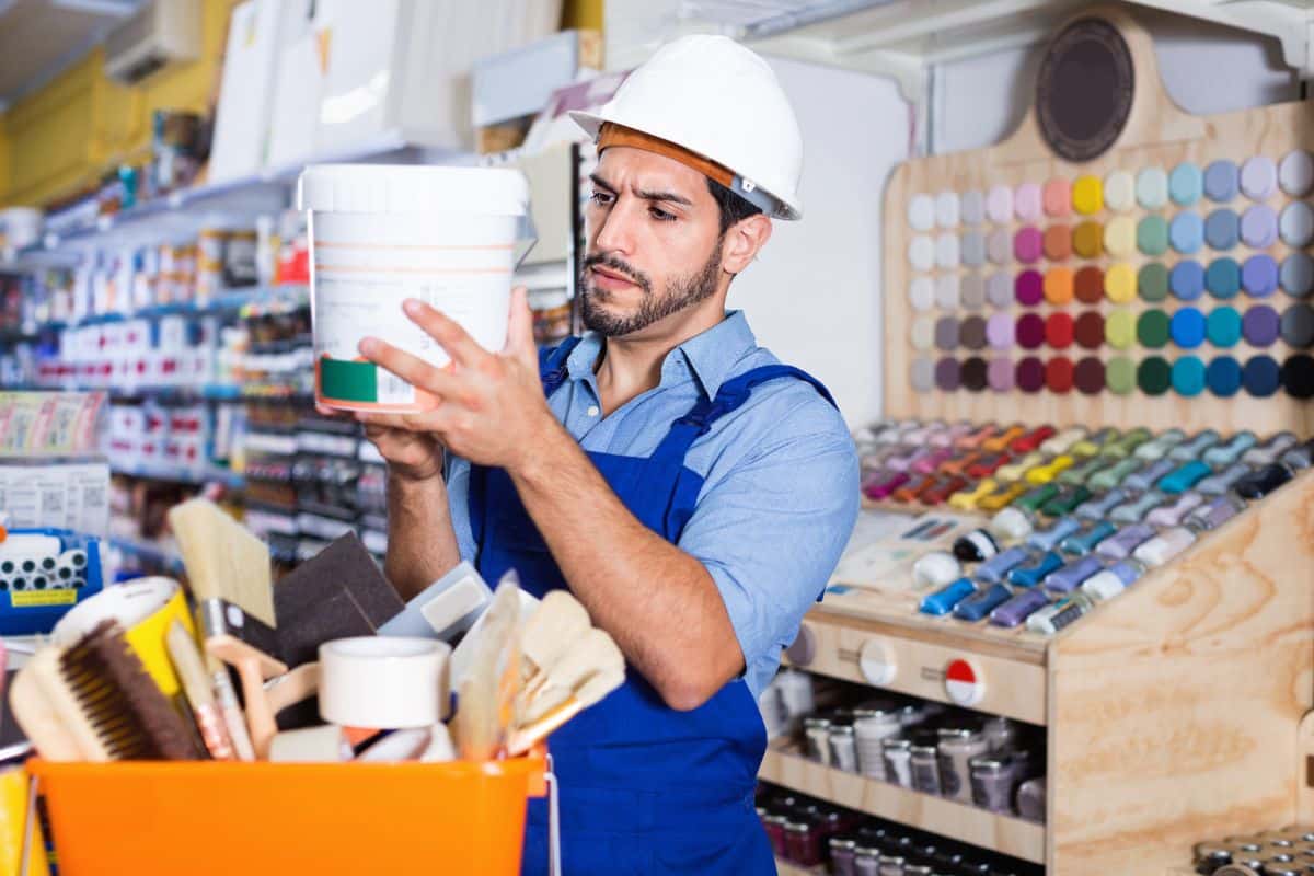 Un homme en casque de travail inspecte de la peinture dans un magasin de matériaux pour travaux de rénovation.