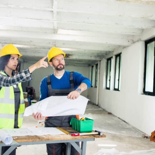 Deux travailleurs en travaux de rénovation portant des casques de protection dans un bâtiment.