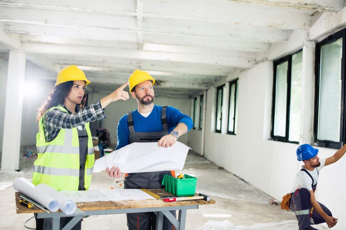 Deux travailleurs en travaux de rénovation portant des casques de protection dans un bâtiment.