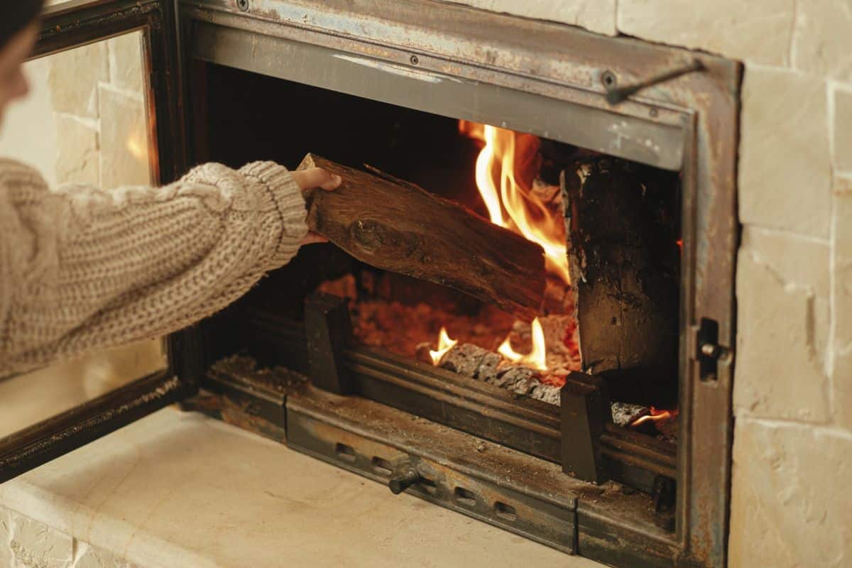 Chauffage d'une maison en hiver avec un poêle à bois. Femme jetant du bois dans une cheminée en feu