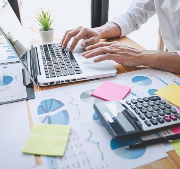 Un Homme Travaillant Sur Un Ordinateur Portable à Un Bureau Avec Des Papiers Et Une Calculatrice.