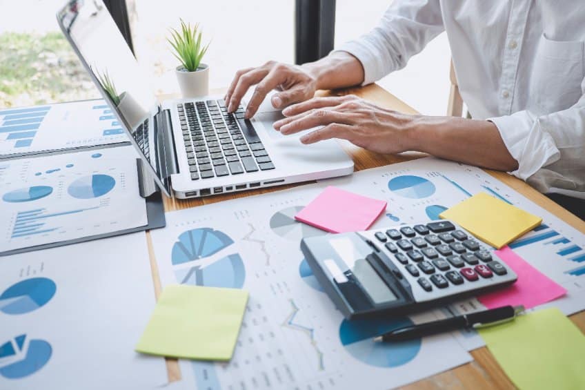 Un Homme Travaillant Sur Un Ordinateur Portable à Un Bureau Avec Des Papiers Et Une Calculatrice.