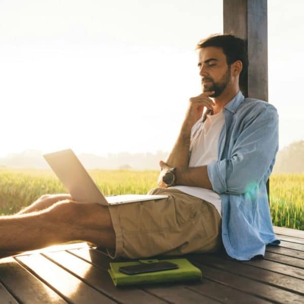 Un Homme Assis Sur Une Terrasse En Bois Avec Un Ordinateur Portable.