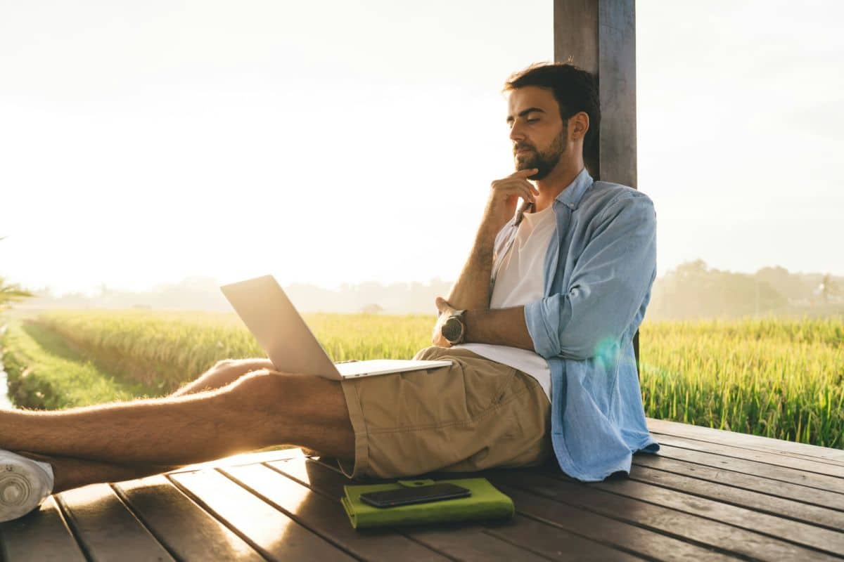 Un Homme Assis Sur Une Terrasse En Bois Avec Un Ordinateur Portable.