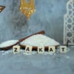 Le mot zakat est écrit sur une planche de bois à côté d’un bol de riz.