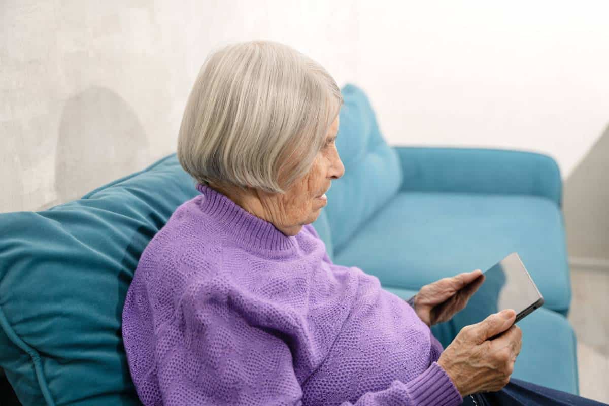 Une Femme âgée Assise Sur Un Canapé à L’aide D’une Tablette.