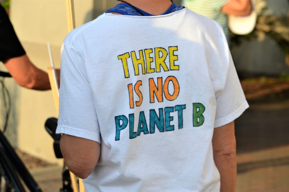 Personne en t-shirt blanc avec le texte « il n'y a pas de planète b » en lettres colorées, vu de dos.