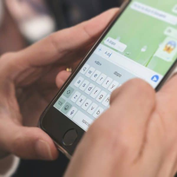 Gros plan des mains envoyant des SMS sur un smartphone, affichant une conversation de chat à l'écran.