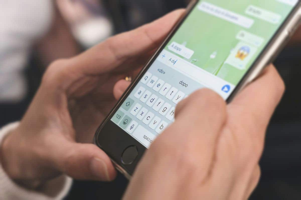 Gros plan des mains envoyant des SMS sur un smartphone, affichant une conversation de chat à l'écran.