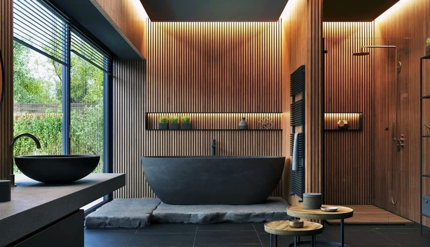 Salle de bains moderne avec boiseries murales, baignoire autoportante noire, miroir circulaire et grandes fenêtres. Cette chambre dispose de plantes d'intérieur, d'un espace douche et d'une décoration minimaliste.
