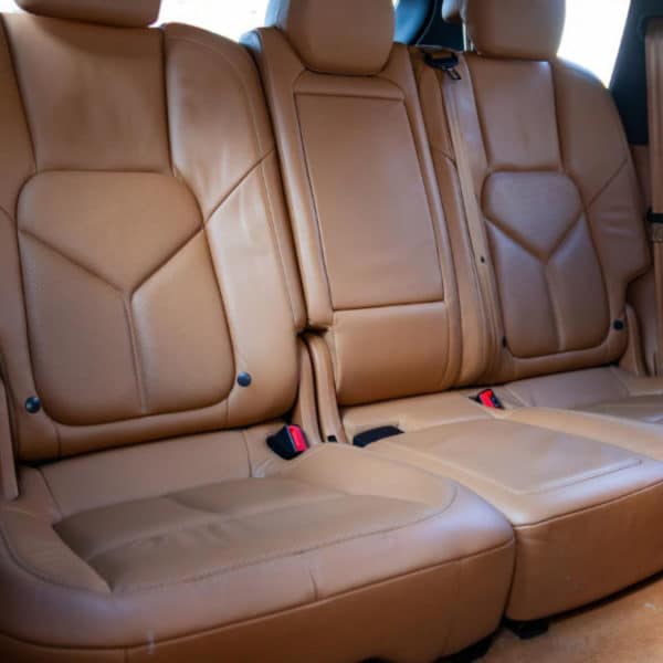 L'image Montre Les Sièges Arrière D'une Voiture. Les Sièges Sont Recouverts De Cuir Beige Et Sont équipés De Ceintures De Sécurité. Un Accoudoir Central Est Replié Contre Le Dossier.
