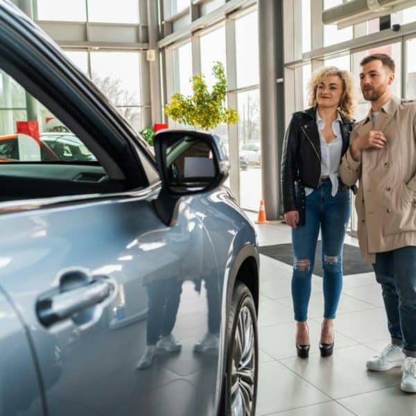 Un Homme Et Une Femme Se Tiennent à L'intérieur D'un Concessionnaire Automobile, Examinant Un Véhicule Bleu.