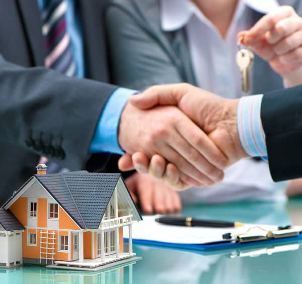 Deux Personnes Se Serrant La Main Devant Un Bureau Avec Une Petite Maquette De Maison, Des Clés Et Un Contrat.