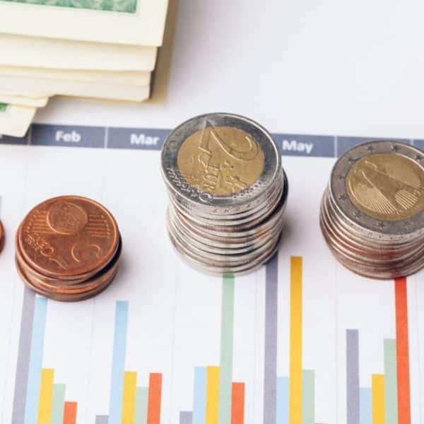 Piles de pièces en euros et de billets de banque en papier sur un graphique à barres financier.
