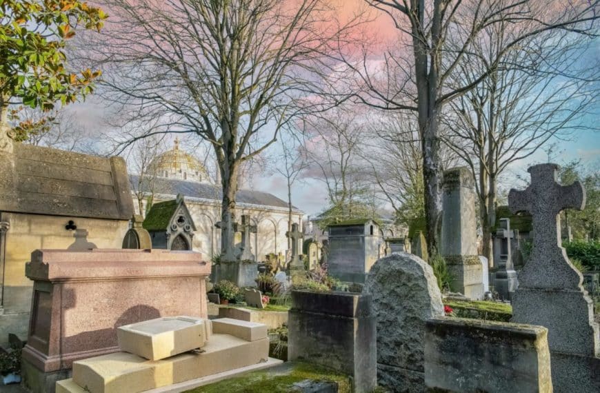 Une Scène De Cimetière Pittoresque Avec Des Pierres Tombales, Des Arbres Nus Et Un Bâtiment En Forme De Dôme En Arrière Plan Sous Un Ciel Coloré.