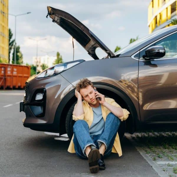 Young man using a mobile phone near a broken car in the city.