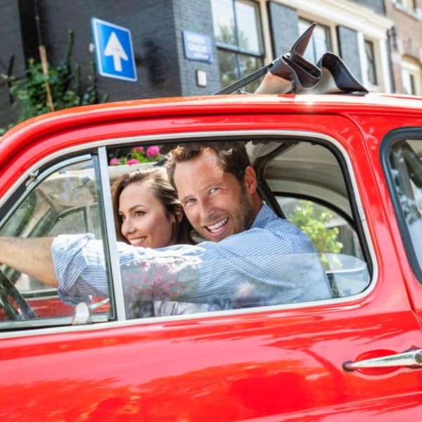 Netherlands, Amsterdam, happy couple with small car in the city