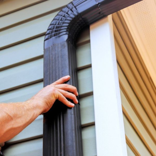 On roof, worker is installing rain gutter fitting a downpipe downspout bend
