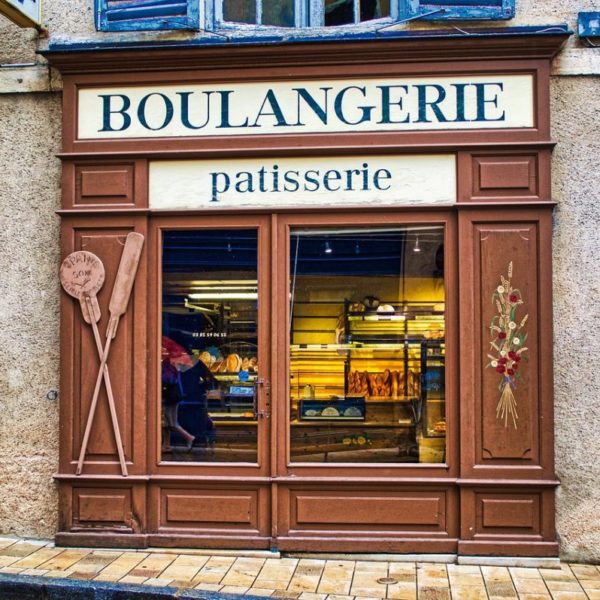 Une Boulangerie Avec Une Enseigne Indiquant « Boulangerie Pâtisserie » Dans Une Rue Rustique. Des Palettes De Cuisson En Bois Sont Exposées à L'extérieur.