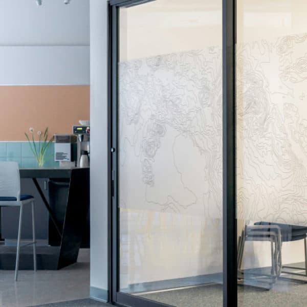 Un Espace De Bureau Moderne Avec Une Porte Vitrée, Des Chaises Blanches, Une Petite Table Et Des œuvres D'art Murales Représentant Des Lignes Abstraites Ressemblant à Des Cartes.